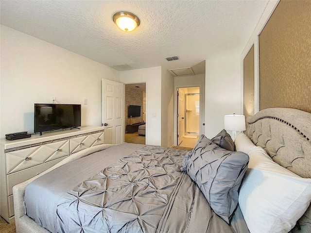 bedroom with visible vents, attic access, light carpet, a textured ceiling, and ensuite bath