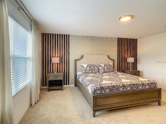 bedroom featuring wallpapered walls, baseboards, light colored carpet, an accent wall, and a textured ceiling