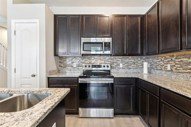 kitchen featuring stainless steel appliances, dark brown cabinetry, and light stone countertops