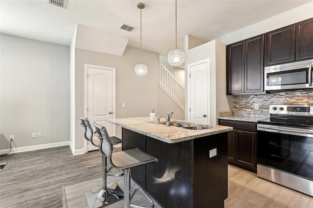 kitchen featuring a breakfast bar, decorative light fixtures, stainless steel appliances, a kitchen island with sink, and a sink