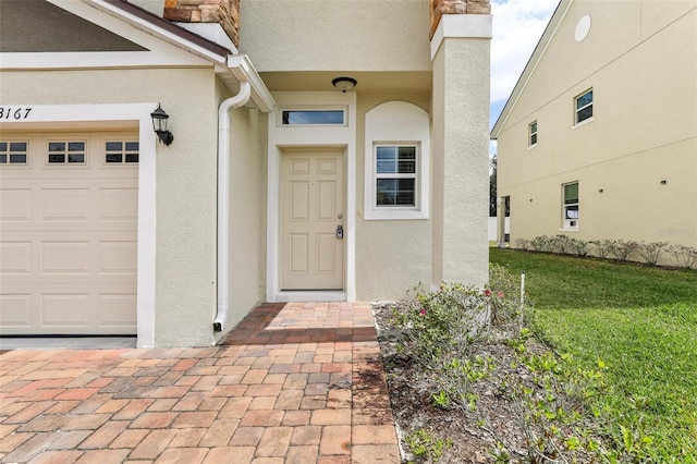 view of exterior entry with an attached garage, a yard, and stucco siding