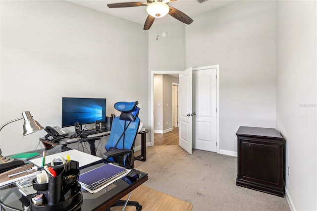 home office with a ceiling fan, light colored carpet, a towering ceiling, and baseboards