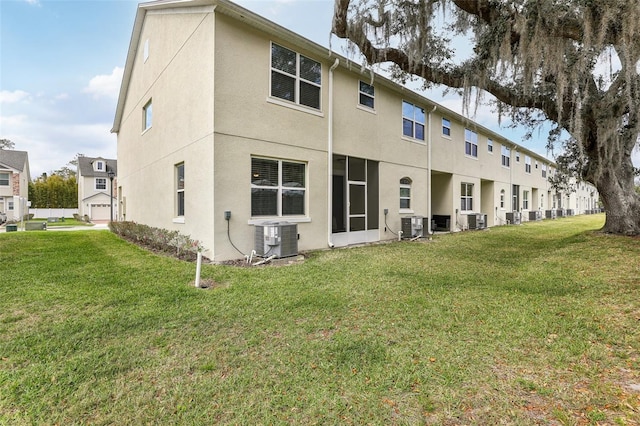 rear view of house featuring central AC unit, a lawn, and stucco siding