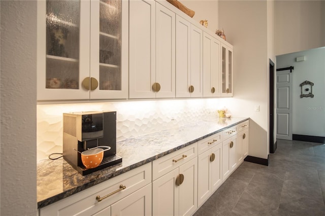 kitchen featuring glass insert cabinets, baseboards, white cabinets, and dark stone countertops