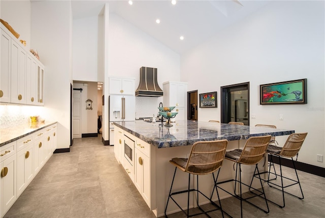 kitchen featuring high vaulted ceiling, a kitchen bar, high end fridge, a spacious island, and premium range hood