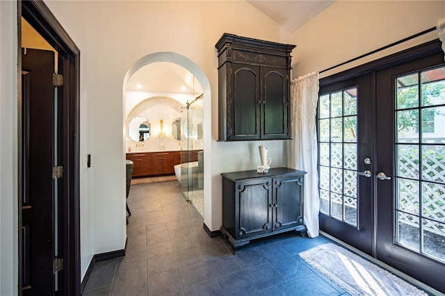 entryway featuring arched walkways, lofted ceiling, french doors, and baseboards