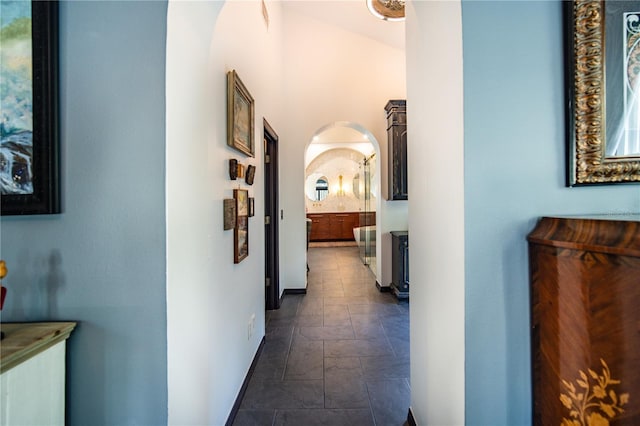 corridor featuring arched walkways, stone finish flooring, and baseboards