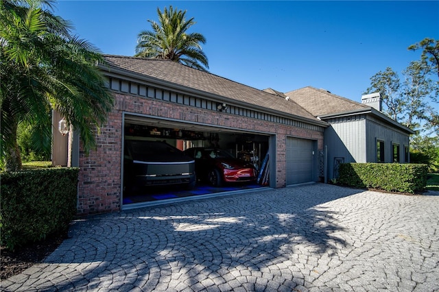 view of property exterior with an attached garage, a chimney, brick siding, and decorative driveway