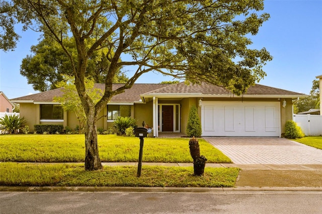 ranch-style house featuring a garage, a front lawn, decorative driveway, and stucco siding