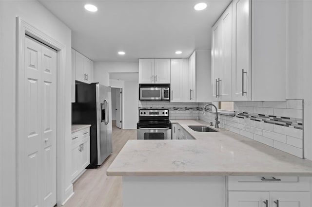 kitchen with appliances with stainless steel finishes, light wood-style floors, white cabinets, a sink, and a peninsula