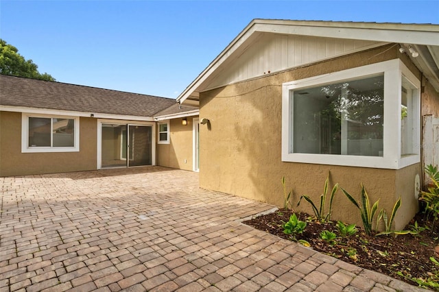 exterior space with stucco siding, a shingled roof, and a patio