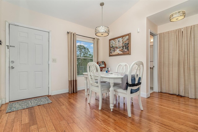 dining space featuring light wood-style floors, baseboards, and vaulted ceiling