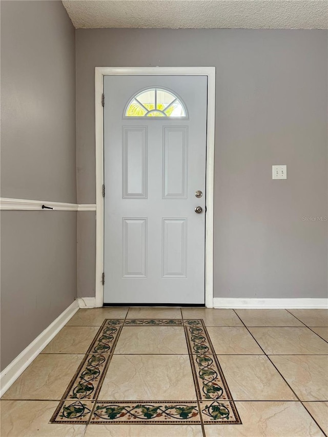 tiled foyer featuring a textured ceiling and baseboards