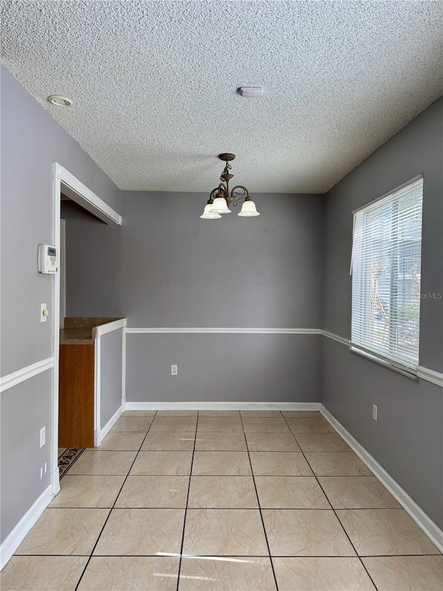 unfurnished dining area with light tile patterned floors, a textured ceiling, baseboards, and an inviting chandelier