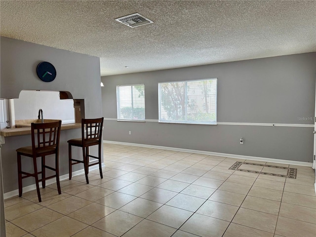 dining area with light tile patterned floors, baseboards, visible vents, and a textured ceiling