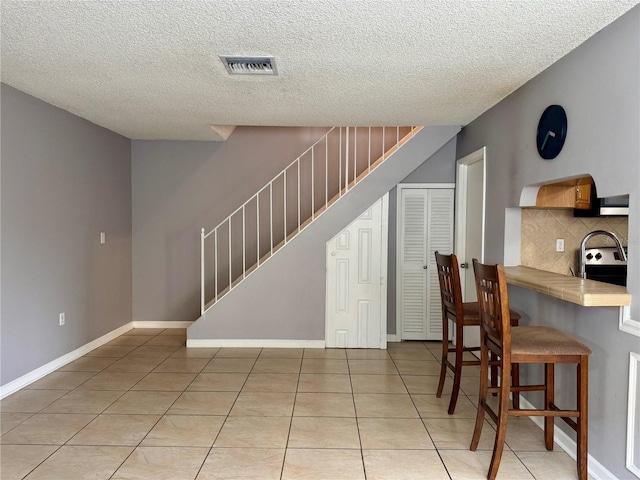 dining area with light tile patterned floors, visible vents, stairway, a textured ceiling, and baseboards