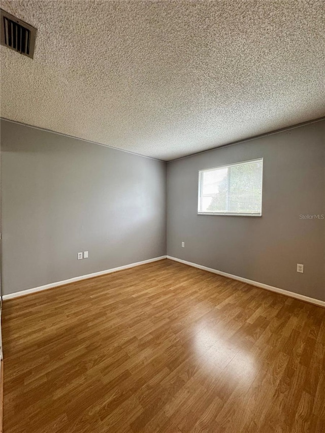 empty room with visible vents, a textured ceiling, baseboards, and wood finished floors