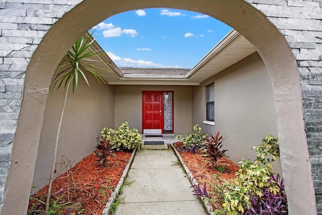 entrance to property featuring a shingled roof and stucco siding