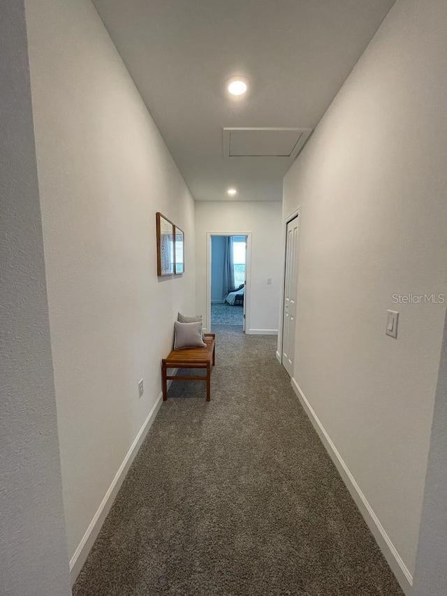 hallway with baseboards, dark carpet, and attic access