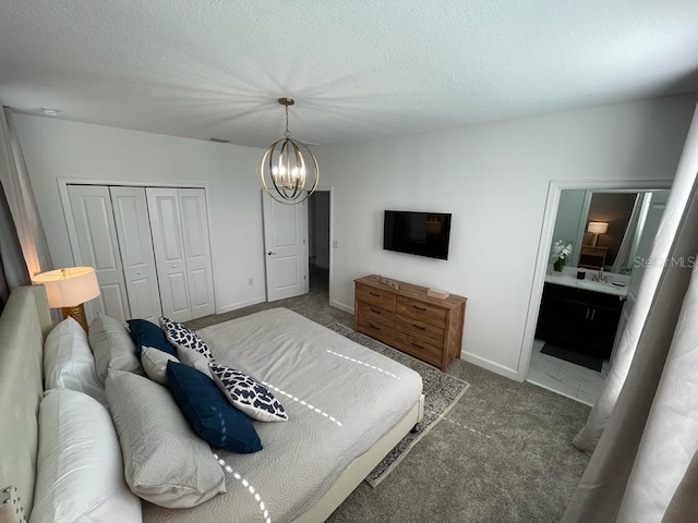 carpeted bedroom with a chandelier, a textured ceiling, baseboards, a closet, and ensuite bath