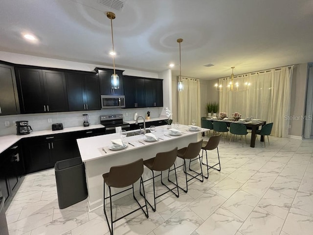 kitchen with dark cabinets, marble finish floor, stainless steel appliances, a kitchen bar, and a sink