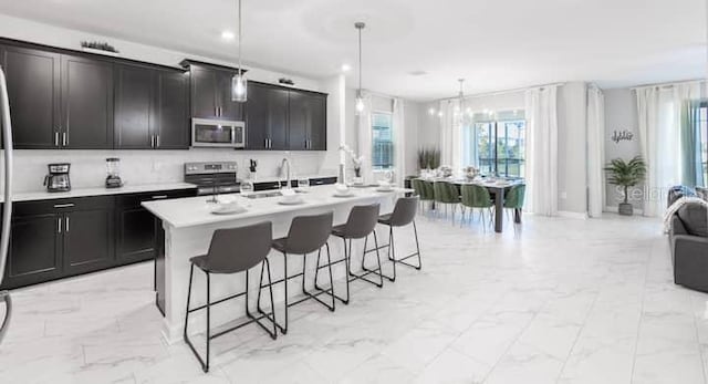 kitchen featuring stainless steel appliances, a breakfast bar, marble finish floor, light countertops, and an island with sink