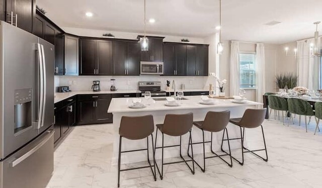 kitchen with decorative backsplash, appliances with stainless steel finishes, a breakfast bar, hanging light fixtures, and marble finish floor