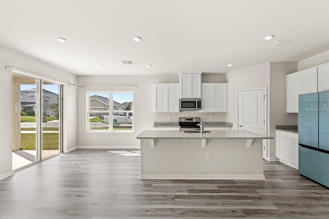 kitchen featuring stainless steel appliances, an island with sink, white cabinets, and light stone countertops