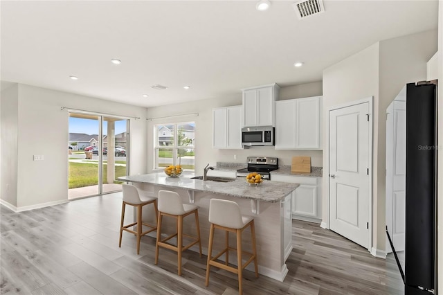 kitchen with stainless steel appliances, visible vents, white cabinets, a kitchen island with sink, and a sink