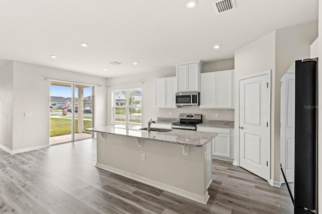 kitchen with appliances with stainless steel finishes, white cabinets, visible vents, and an island with sink