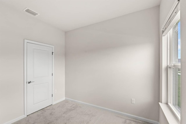 spare room with light colored carpet, visible vents, and baseboards