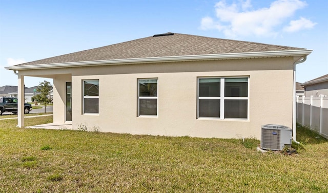 back of property with stucco siding, cooling unit, a lawn, and roof with shingles