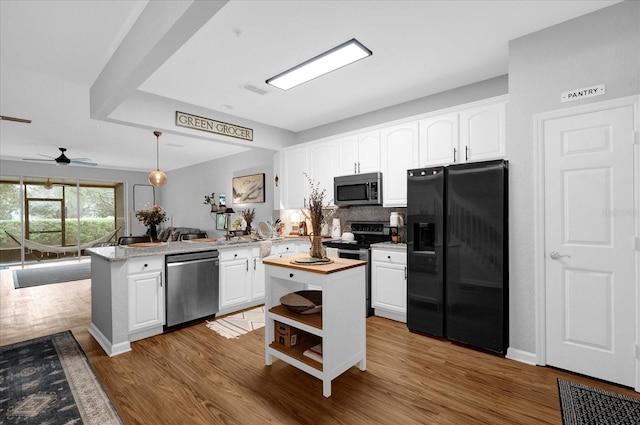 kitchen with stainless steel appliances, a peninsula, white cabinetry, a center island, and decorative light fixtures