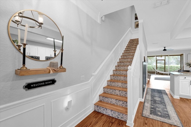 stairs with wainscoting, visible vents, a decorative wall, and wood finished floors