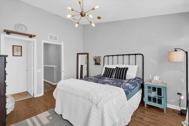 bedroom with baseboards, wood finished floors, visible vents, and an inviting chandelier