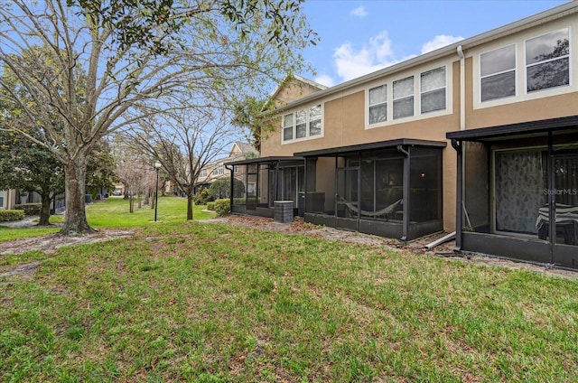 back of house featuring a lawn, a sunroom, and stucco siding