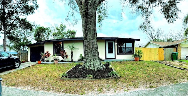 ranch-style home with an attached garage, a front yard, concrete driveway, and stucco siding