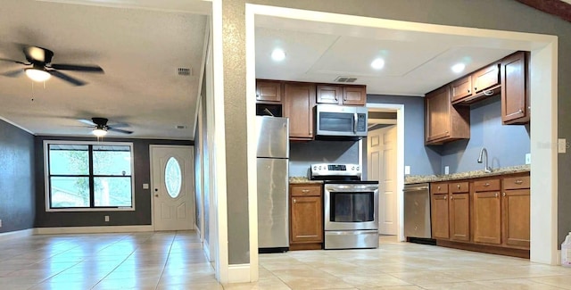 kitchen featuring visible vents, brown cabinetry, a ceiling fan, light stone counters, and stainless steel appliances