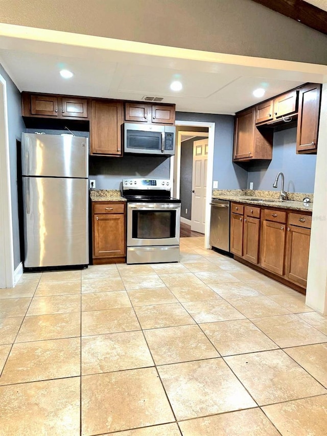 kitchen featuring appliances with stainless steel finishes, a sink, light stone counters, and light tile patterned floors