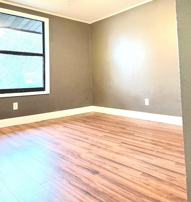 empty room with ornamental molding, light wood-style flooring, and baseboards