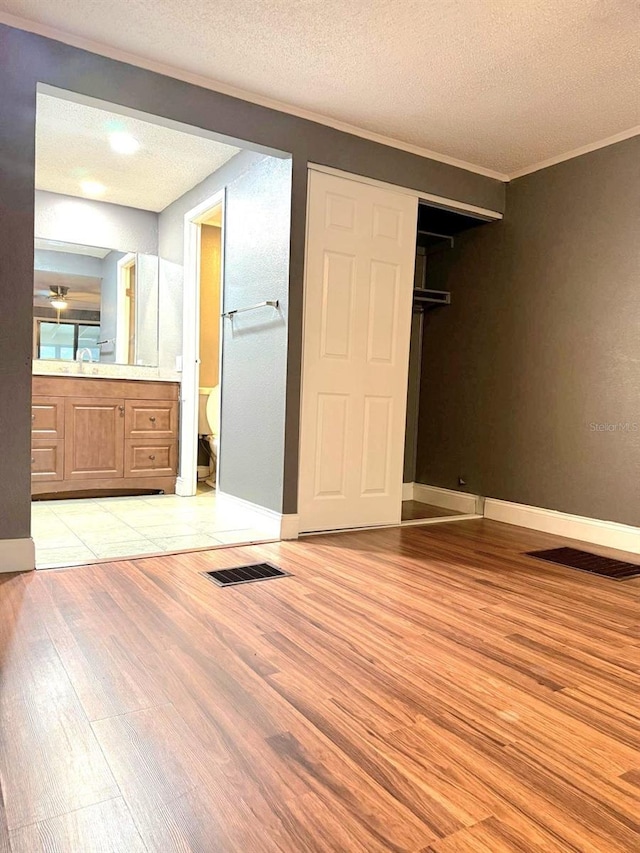 unfurnished bedroom featuring ornamental molding, light wood finished floors, a textured ceiling, and visible vents