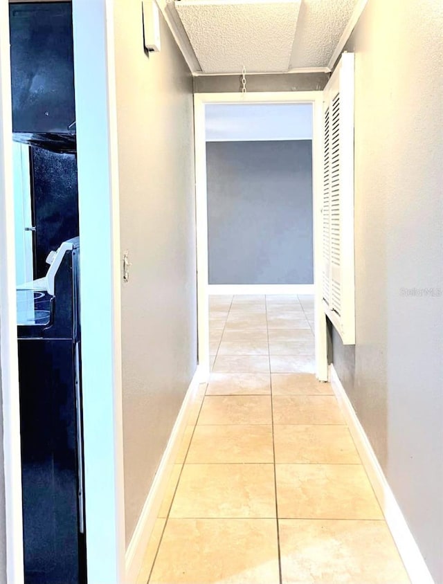 hall featuring light tile patterned flooring, a textured ceiling, and baseboards