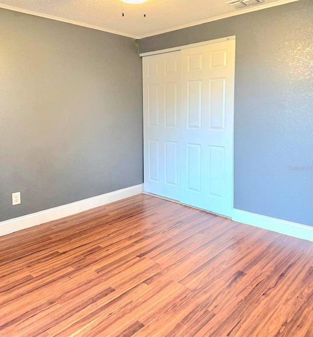 unfurnished bedroom with a textured ceiling, baseboards, ornamental molding, a closet, and light wood finished floors