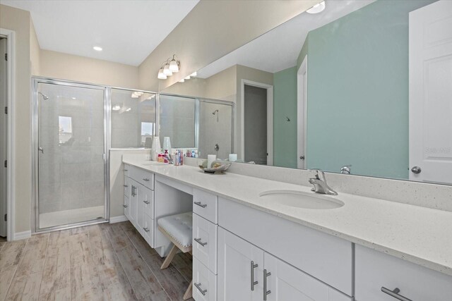 full bathroom with double vanity, a stall shower, a sink, and wood finished floors