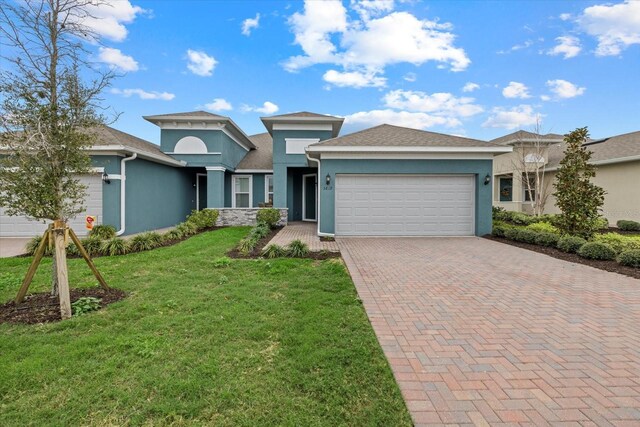 view of front facade with a front yard, decorative driveway, an attached garage, and stucco siding