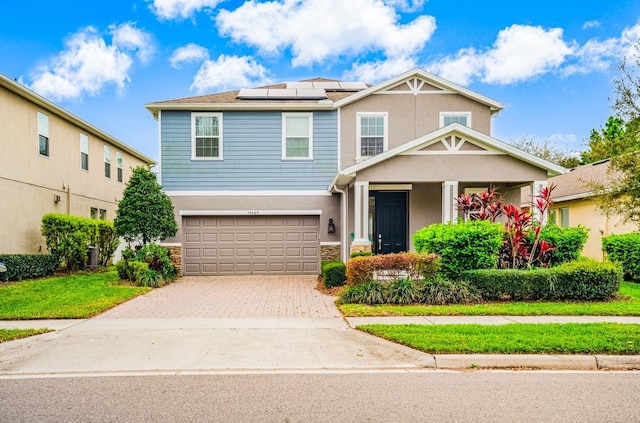 craftsman-style home with stucco siding, an attached garage, decorative driveway, roof mounted solar panels, and a front yard