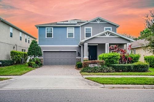 view of front of property featuring a garage, roof mounted solar panels, driveway, and a front lawn