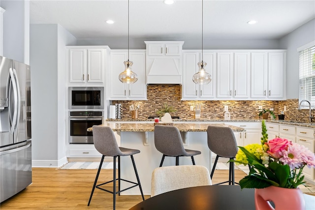 14664 Spotted Sandpiper Blvd, Winter Garden, FL 34787 - kitchen with stainless steel appliances, light wood-style flooring, white cabinets, a breakfast bar, and backsplash
