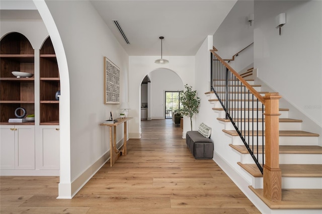 entryway featuring arched walkways, light wood finished floors, stairs, and baseboards