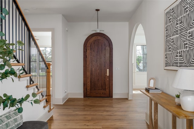 entryway with arched walkways, light wood finished floors, stairs, and baseboards